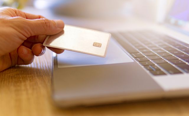 person holding a credit card over a laptop